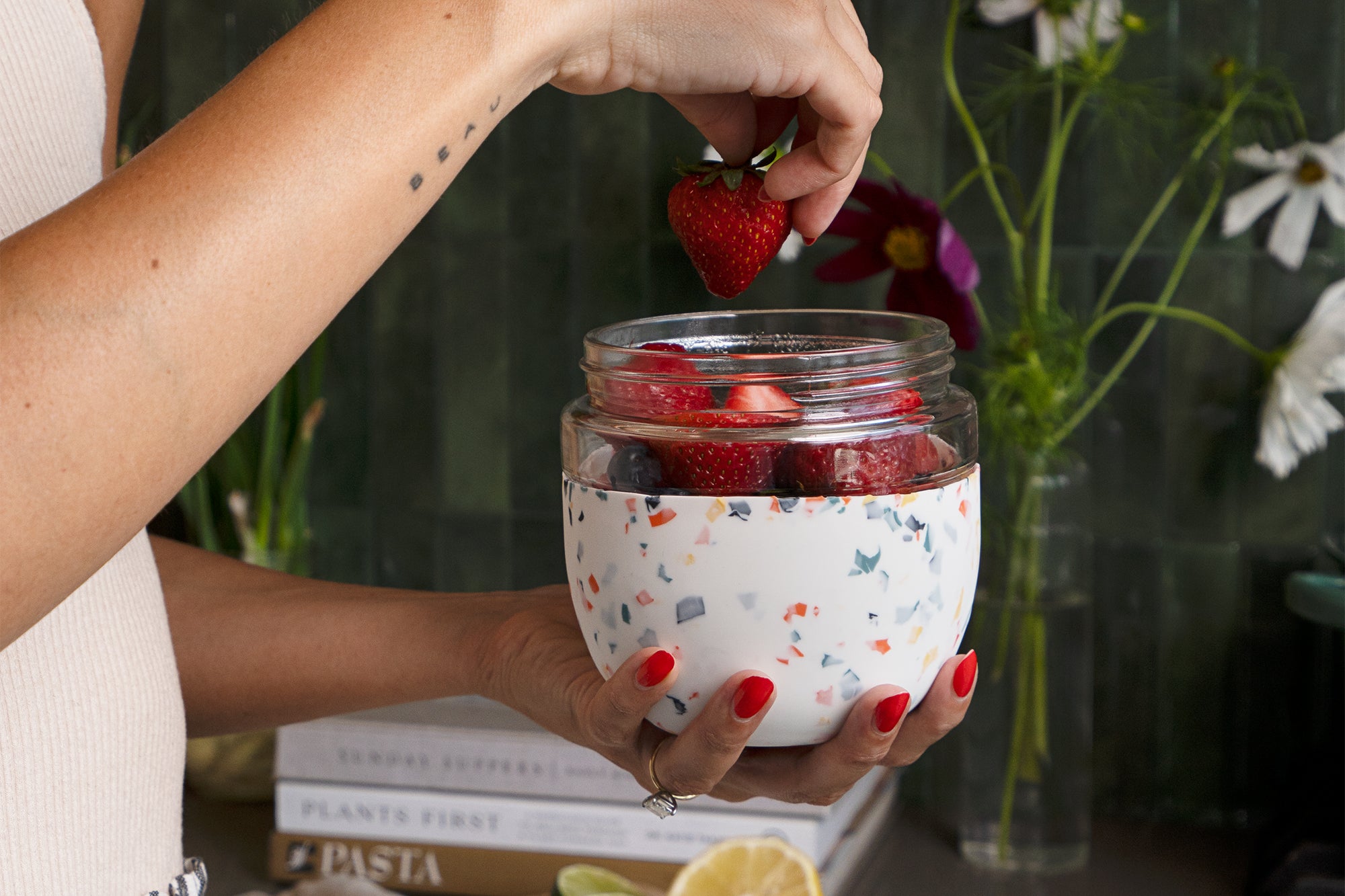 Hand adding strawberries to a W&P Seal Tight Bowl in Terrazzo Cream filled with yogurt