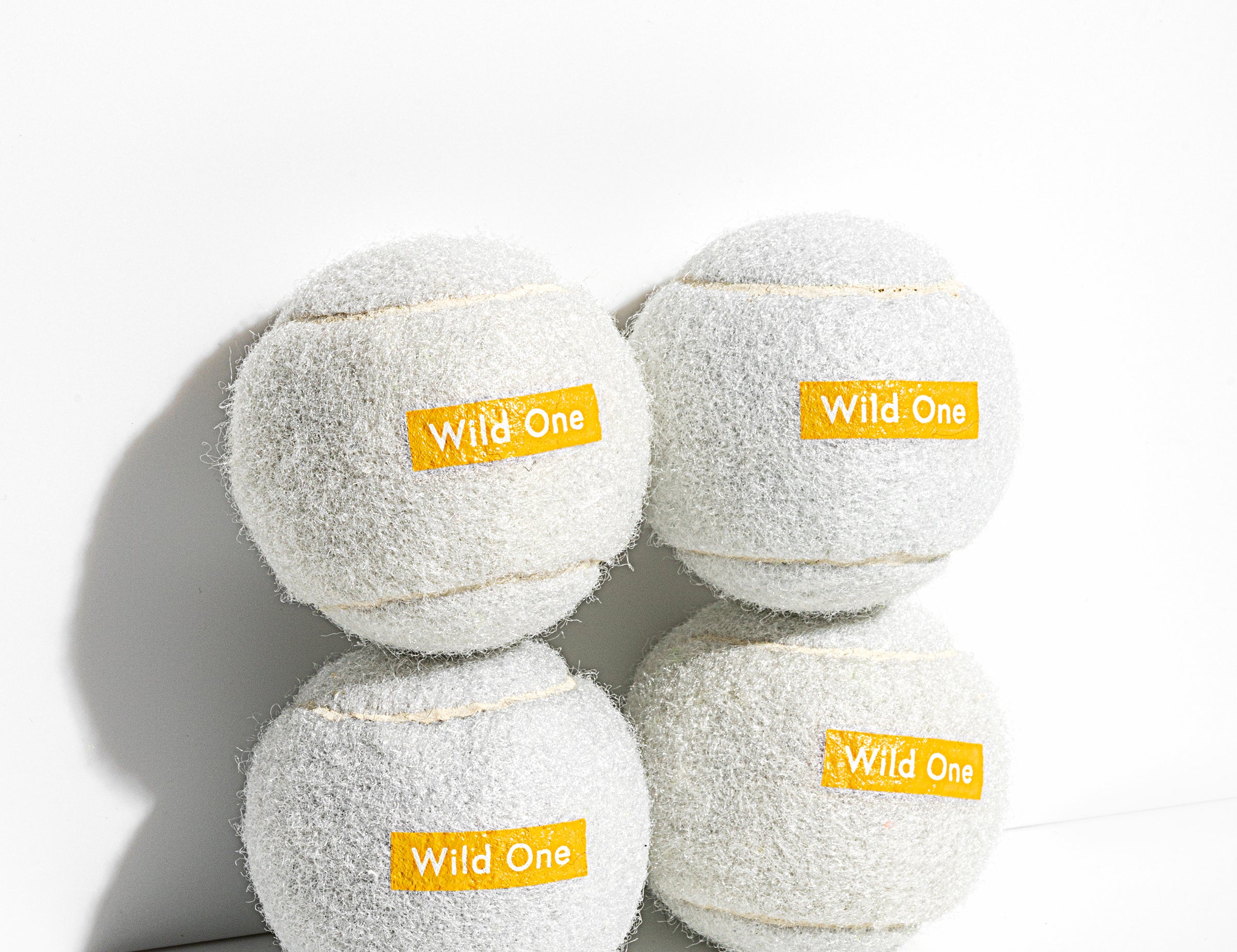 Wild One Tennis Balls in White, four white felt balls stacked with an orange Wild One logo
