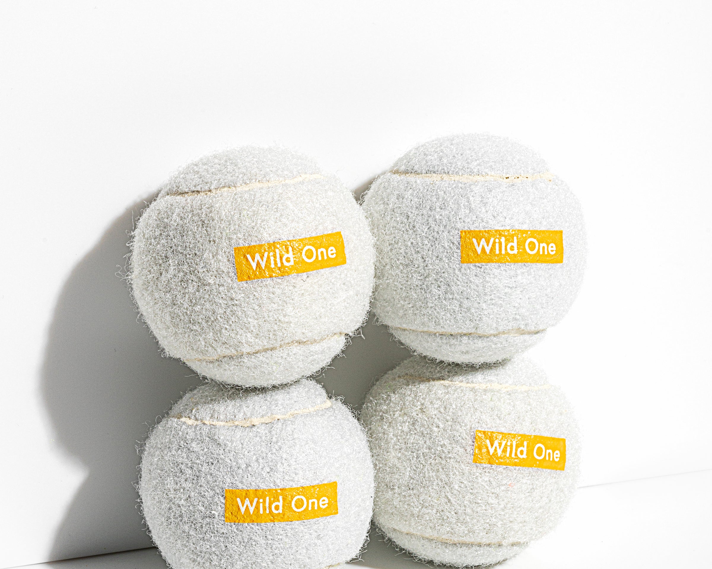 Wild One Tennis Balls in White, four white felt balls stacked with an orange Wild One logo