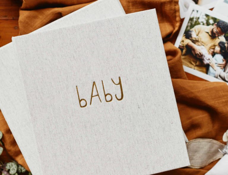 Write to Me Grey The First Year of You baby book, a linen cover with embroidered baby lettering, on a rust blanket