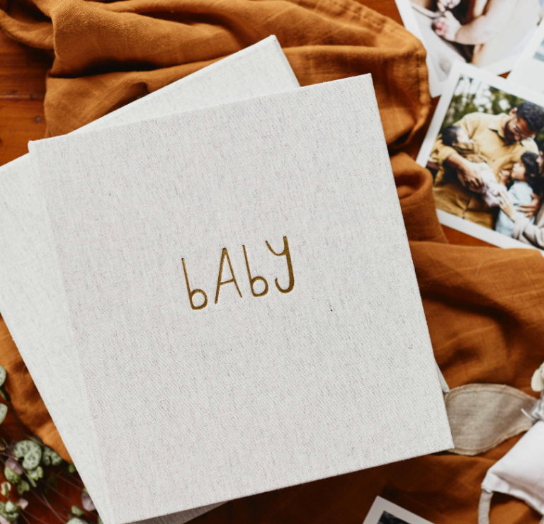 Write to Me Grey The First Year of You baby book, a linen cover with embroidered baby lettering, on a rust blanket